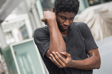 african man suffering from elbow pain; sick black man with elbow joint pain, osteoporosis, bone arthritis, gout, symptoms; body sickness, health care or pain concept; adult african man or model