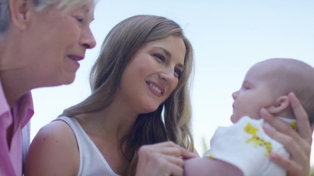 Mother and grandmother playing with infant baby outdoors, in slow motion