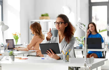 business, technology and people concept - african american businesswoman with tablet pc computer drinking coffee at office