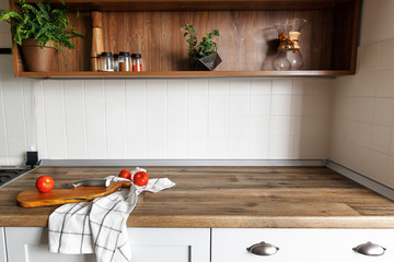 wooden board with knife, tomatoes on modern kitchen countertop and shelves with ingredients spices...