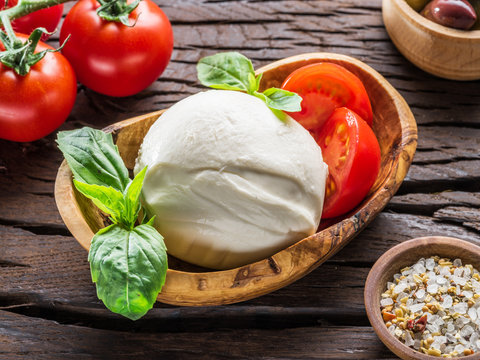 Buffalo mozzarella in the wooden bowl and cherry tomatoes on the table.