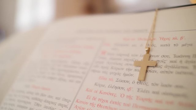 Close up of an open Greek bible with a cross necklace draped over it