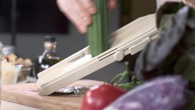 Tracking shot of chef slicing fresh cucumber using mandolin