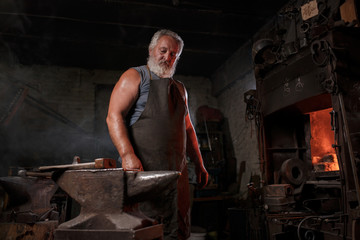 Portrait of a blacksmith artisan in an apron with an anvil in a blacksmith