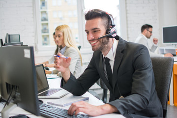 Smiling business man with headset working on desktop computer in customer service support center