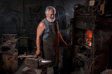 Portrait of a blacksmith artisan in an apron with an anvil in a blacksmith