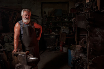 Fototapeta na wymiar Portrait of a blacksmith artisan in an apron with an anvil in a blacksmith