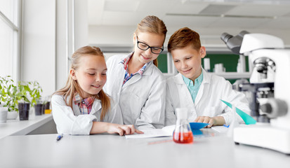 Fototapeta premium education, science and children concept - happy kids with workbooks studying chemistry at school laboratory