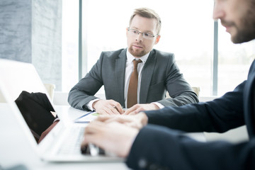 Portrait of  young businessman wearing glasses talking to partner using laptop in meeting, copy space