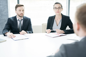 Portrait of two successful business people, man and woman,  talking to partner sitting across meeting table and negotiating  in conference room, copy space
