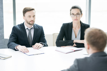 Portrait of two business people, man and woman,  talking to partner sitting across meeting table in conference room, copy space
