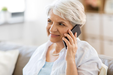 technology, communication and people concept - happy senior woman calling on smartphone at home