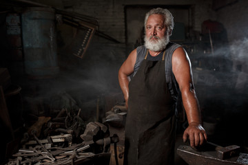 Portrait of a brutal blacksmith artisan in an apron in a blacksmith