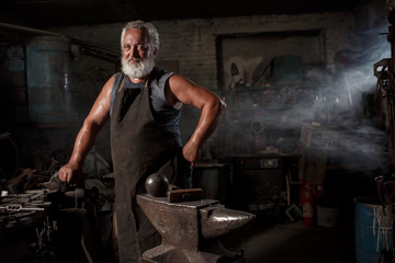 Portrait of a brutal blacksmith artisan in an apron in a blacksmith