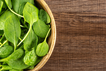 Fresh baby spinach leaves in a wooden bowl top view on brown wood background.
