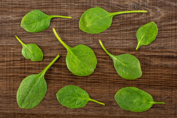 Fresh baby spinach leaves top view on brown wood background.