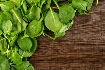 Fresh baby spinach leaves top view on brown wood background left upper corner.