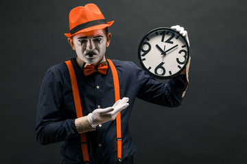 scary clown pantomime with a clock in his hands, on a dark background