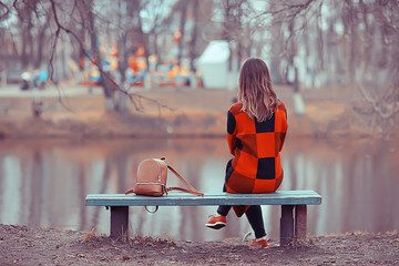 girl bench pond autumn / concept lonely girl in autumn relaxes near a pond on a garden bench,...