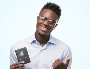 Young african american man holding australian passport pointing with hand and finger up with happy face smiling