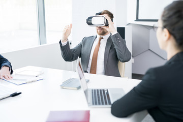Fototapeta premium Portrait of contemporary businessman using VR while sitting at meeting table in conference room, copy space