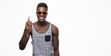 Young african american man wearing sunglasses surprised with an idea or question pointing finger...