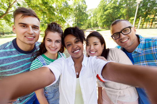 people, friendship and international concept - happy smiling young woman and group of happy friends taking selfie outdoors
