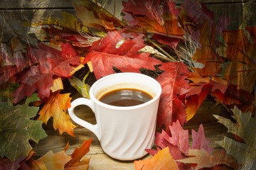 A single hot cup of coffee encircled by leaves in autumn colors on a wooden surface with a texture applied to the fringes of the image.