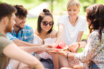 friendship, leisure and summer concept - group of happy friends eating watermelon at picnic in park