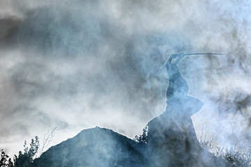 Silhouette of a warrior with a sword in the smoke of a mountain war © kichigin19