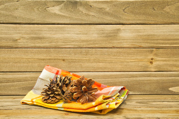 A still life of an autumn colored napkin and pine cones on wood providing copy space.