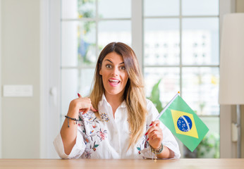 Young woman at home holding flag of Brazil with surprise face pointing finger to himself