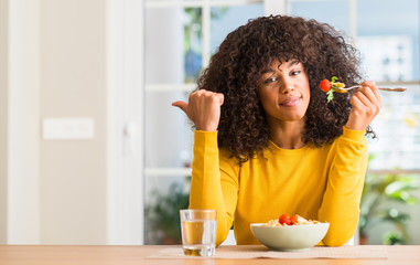 African american woman eating pasta salad at home pointing with hand and finger up with happy face...