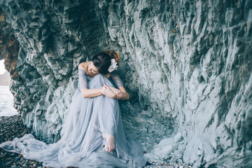 A woman in a long dress sitting near the sea