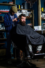 Barber with clipper trimming hair on nape of client. Hipster client getting haircut. Hipster hairstyle concept. Barber with hair clipper works on haircut of bearded guy barbershop background