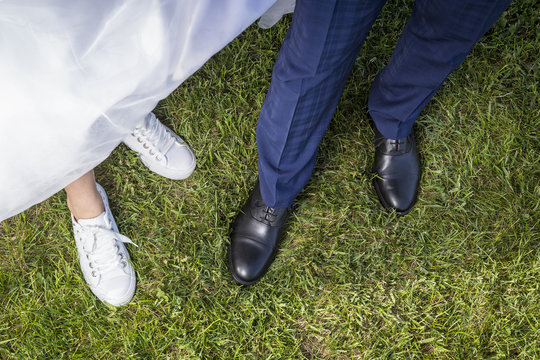 legs and shoes of bride and groom on green grass. white sneakers and black formal shoes, bridal accessories.
