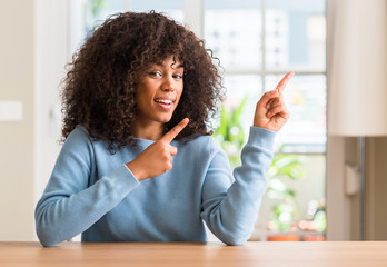 African american woman at home smiling and looking at the camera pointing with two hands and...