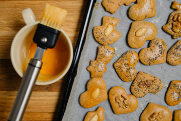 Gingerbread with nuts on baking tin and a brush with eggs in a cup