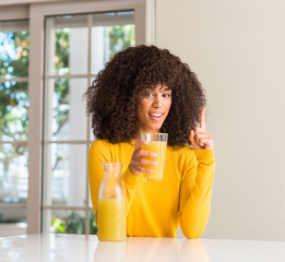 African american woman drinking healthy fruit juice at home surprised with an idea or question pointing finger with happy face, number one