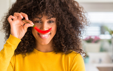 African american woman eating red hot chili pepper with a happy face standing and smiling with a...