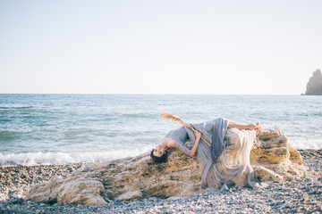 Beautiful sexy woman in a long dress of voila lies on a big stone near the sea