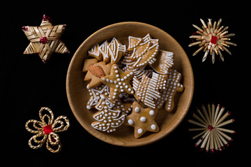 Fototapeta premium Various shapes of fresly baked ginderbread in a wooden bowl and straw decorations in corners