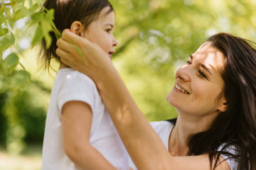 Caucasian beautiful mother and her cute kid playing outdoors, holding each other. Pretty woman and her child girl enjoy the time together in the park. People, motherhood