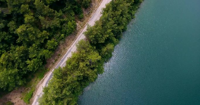 Aerial View. Flying over the beautiful lake and forest way. Sunny Day. Aerial camera shot. Landscape panorama.