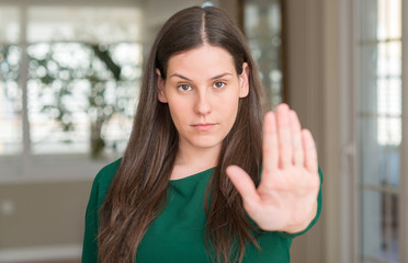 Young beautiful woman at home with open hand doing stop sign with serious and confident expression, defense gesture