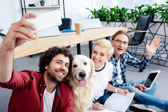 smiling young people taking selfie with labrador in office