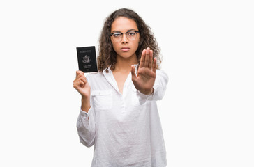 Fototapeta premium Young hispanic woman holding passport of United States of America with open hand doing stop sign with serious and confident expression, defense gesture