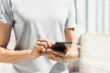 Young man texting on his smartphone in the city. Close up of hand using mobile phone outdoor