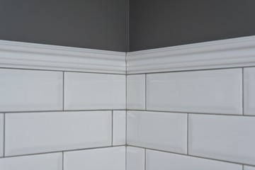 Gray painted wall, part of the wall is covered tiles small white glossy brick, ceramic decorative...