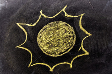 Yellow color chak hand drawing in sun with ray shape on blackboard background